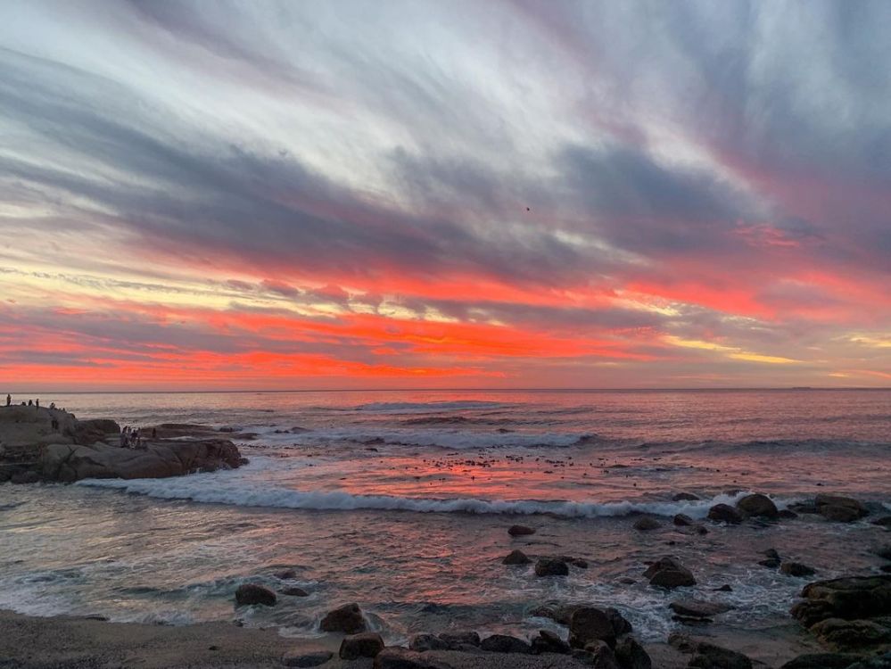 Stunning sunset over the ocean with vibrant orange and pink hues blending in the sky, captured at a rocky beach in Cape Town.