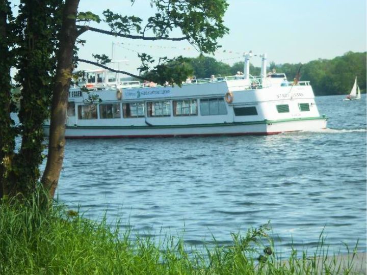 A scenic view of a boat sailing on Lake Baldeney in Essen, surrounded by greenery and trees.