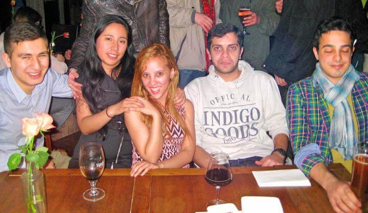 Group of five friends sitting at a table in a social setting, smiling and enjoying their time together.