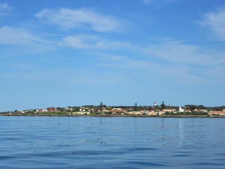 View of Robben Island from the ferry, showcasing the coastline, buildings, and clear blue sky.