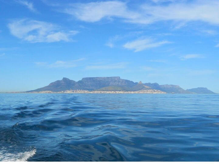 A view of Table Mountain and the city of Cape Town from a ferry on the water, with clear blue skies and calm sea.