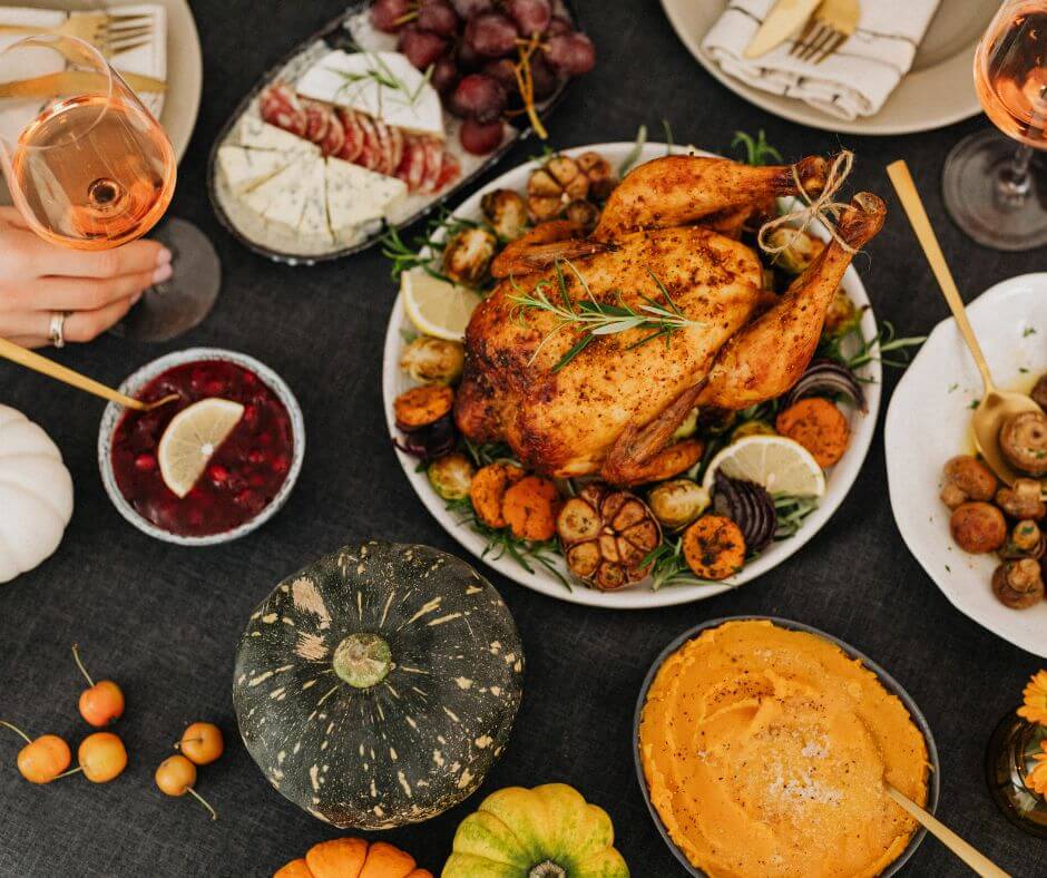 A beautifully arranged Thanksgiving table featuring a roasted turkey surrounded by seasonal vegetables, cranberry sauce, and side dishes, with glasses of rose wine and decorative pumpkins.
